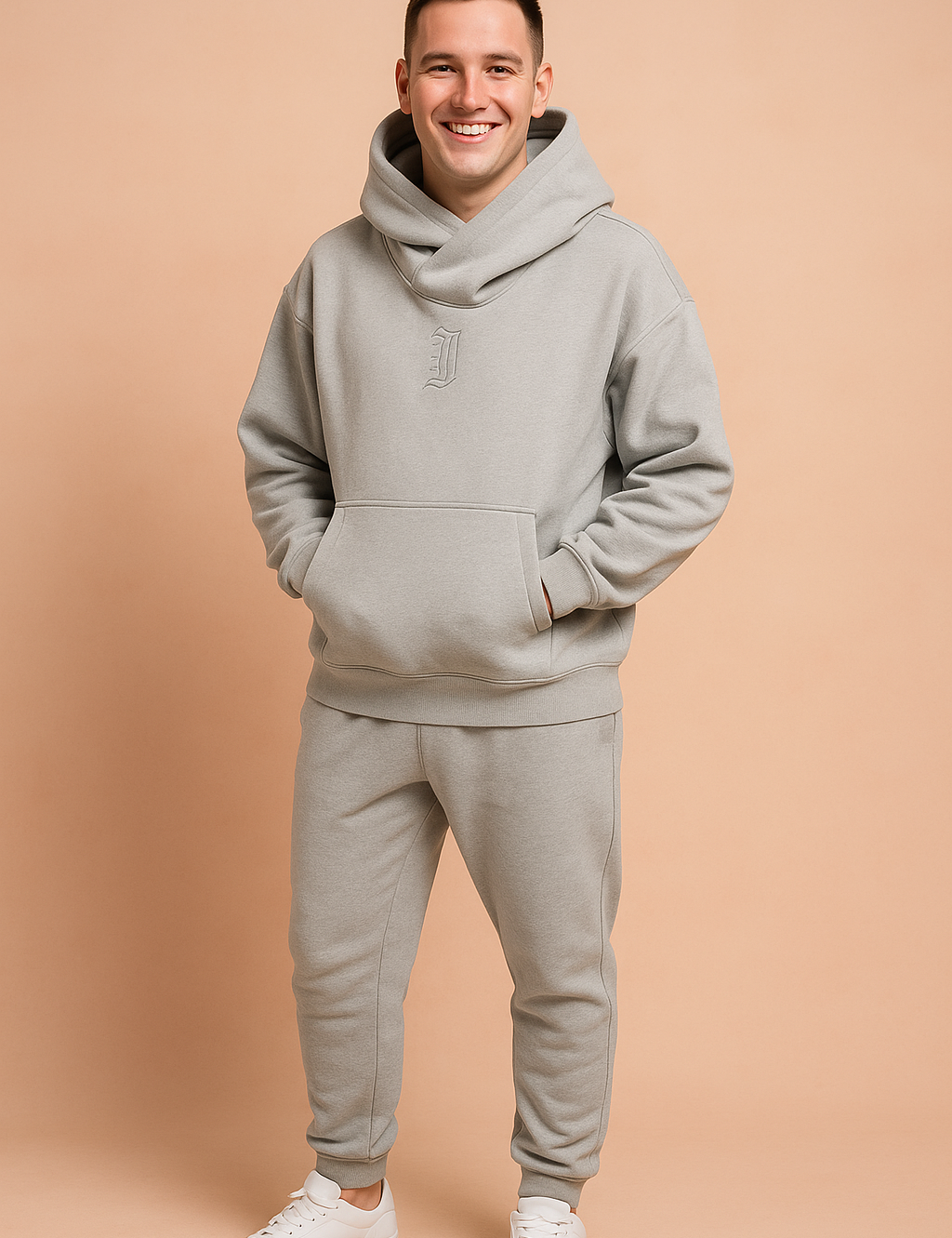 Light grey oversized hoodie with a wide cowl neck and subtle embroidered "J" detail, paired with matching jogger pants and white sneakers, styled for modern streetwear comfort.