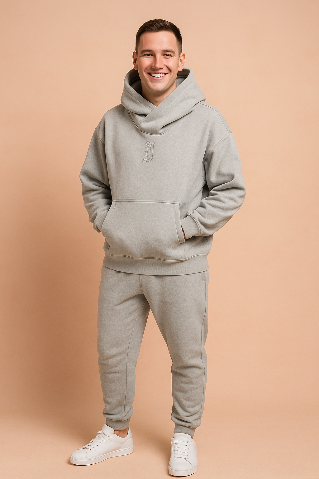Light grey oversized hoodie with a wide cowl neck and subtle embroidered "J" detail, paired with matching jogger pants and white sneakers, styled for modern streetwear comfort.