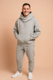 Light grey oversized hoodie with a wide cowl neck and subtle embroidered "J" detail, paired with matching jogger pants and white sneakers, styled for modern streetwear comfort.