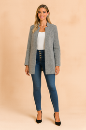 Grey herringbone longline jacket paired with a white top, dark blue high-waisted skinny jeans, and black suede heels, styled in a modern casual fashion look