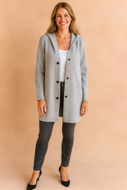 Light grey hooded longline coat with front button closure, styled over a white top and paired with fitted dark jeans and black heels for a sleek everyday look.