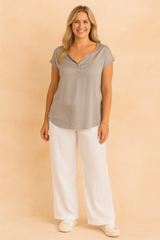 Short-sleeve light grey satin blouse with a soft split neckline and three-button placket, paired with white wide-leg trousers and white sneakers.
