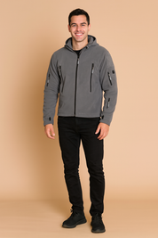 Grey softshell jacket with hood, multiple zippered pockets, and long sleeves with thumbholes, styled with black jeans and sneakers.