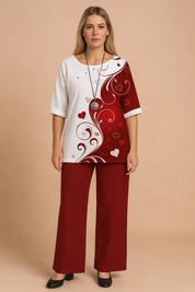 Two-piece set featuring a half-and-half heart swirl print top in white and deep red with short sleeves and side button detail, paired with solid dark red wide-leg trousers in soft cotton-blend fabric.