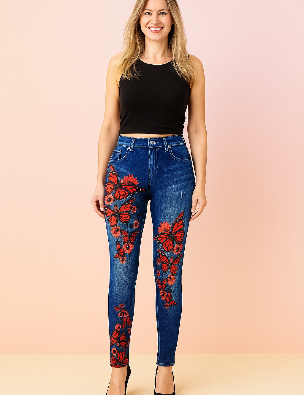 High-waisted skinny jeans in medium blue denim with vivid red butterfly and floral print detailing along the thighs and legs, styled with a sleek black sleeveless top and classic black pointed-toe heels