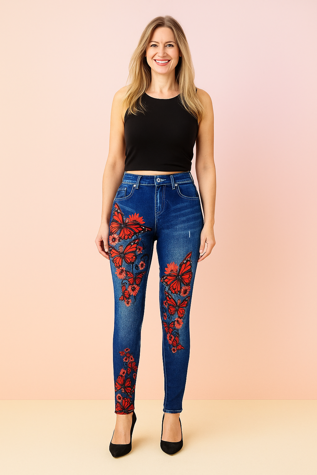 High-waisted skinny jeans in medium blue denim with vivid red butterfly and floral print detailing along the thighs and legs, styled with a sleek black sleeveless top and classic black pointed-toe heels
