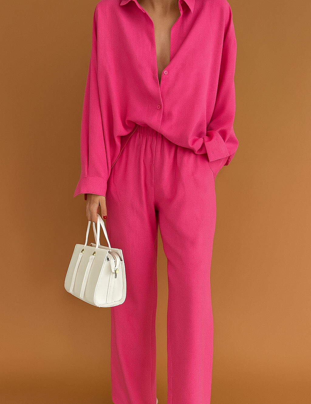 Oversized hot pink co-ord set featuring a button-down shirt with a relaxed collar and full-length straight-cut pants, paired with a structured white handbag.
