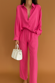 Oversized hot pink co-ord set featuring a button-down shirt with a relaxed collar and full-length straight-cut pants, paired with a structured white handbag.