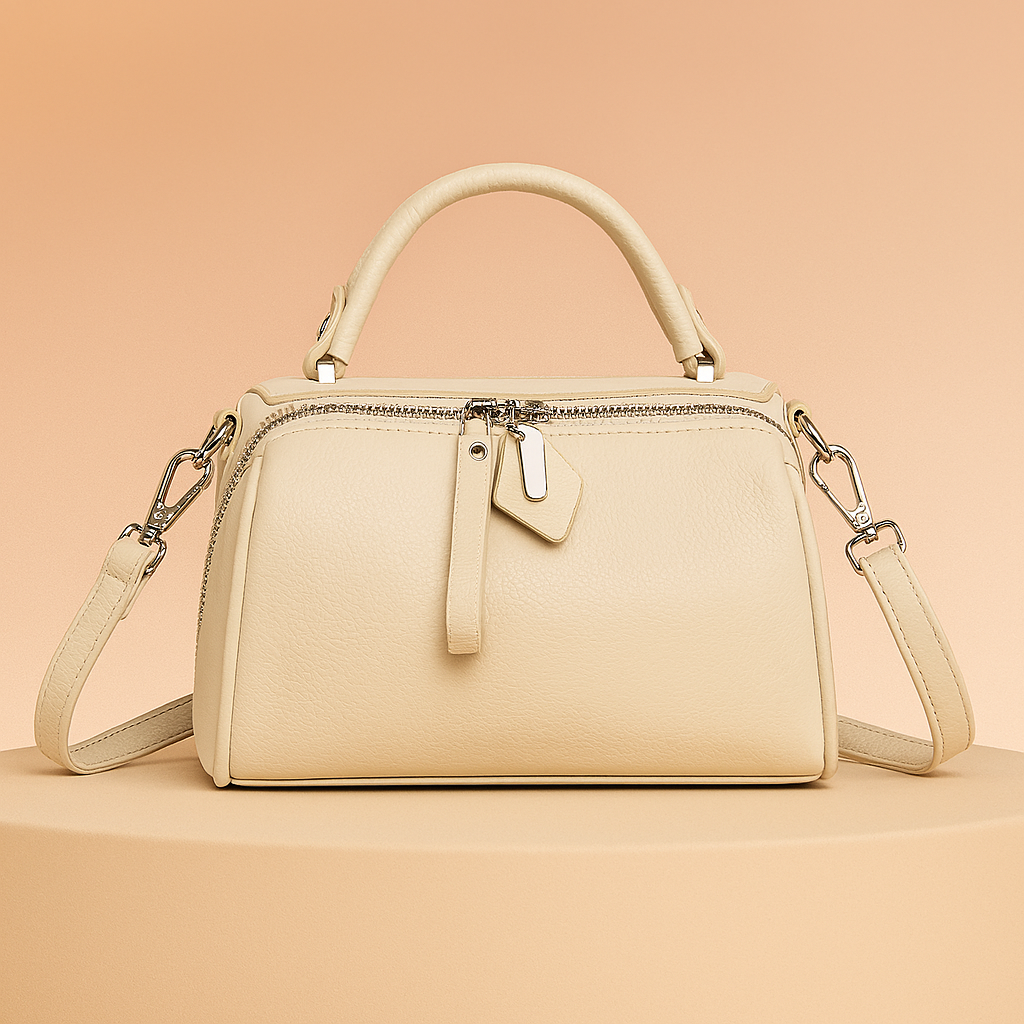 Ivory leather handbag with top handle, silver zipper, leather tag detail, and detachable shoulder strap on a warm gradient platform.