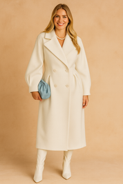 Chic ivory double-breasted long coat with structured sleeves, tailored waistline, and matching ivory boots, styled with a soft blue clutch.