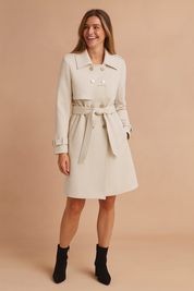 Elegant double-breasted ivory trench coat with belted waist, adjustable cuff straps, and six front buttons, crafted in smooth fabric for a refined finish.