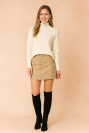 : Ivory turtleneck sweater paired with a beige mini skirt and black knee-high boots, featuring a clean minimalist design with smooth fabric texture and tailored seams.