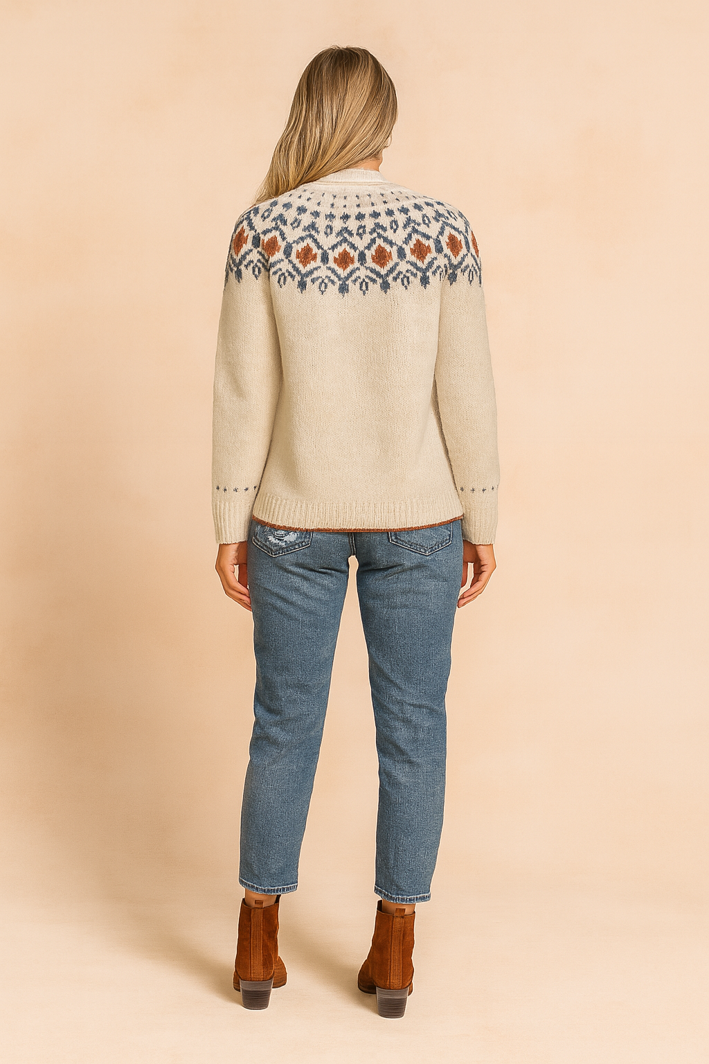 Beige knit sweater with multicolor Nordic-inspired geometric pattern across chest and cuffs, paired with distressed blue jeans and brown suede ankle boots.
