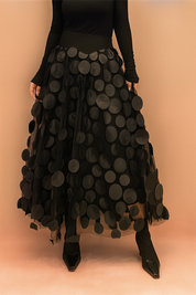 Laura – Elegant black summer skirt featuring large circular appliqués, styled with a fitted black top and boots, perfect for bold fashion statements in a chic editorial setting.