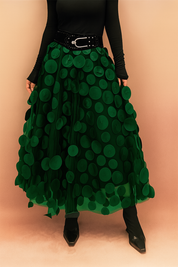 Laura – Elegant dark green summer skirt featuring large circular appliqués, styled with a fitted black top and boots, perfect for bold fashion statements in a chic editorial setting.