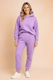 Lavender fleece loungewear set consisting of a cozy hooded sweatshirt with a slightly oversized fit and elastic-waist jogger pants, paired with minimalist white sneakers for a soft casual look.

