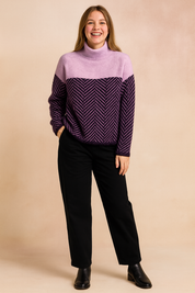 Two-tone knit sweater with a soft pastel lavender upper and a deep purple herringbone-patterned lower section, designed with a relaxed fit, long sleeves, and a cozy high neckline, paired with classic black trousers and ankle boots.