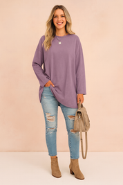 Oversized lavender long-sleeve tunic paired with light blue distressed skinny jeans, taupe ankle boots, and a matching taupe handbag.