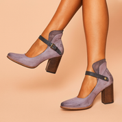 Lavender suede block-heel Mary Jane shoes featuring a dark leather strap with brass buckle, high-cut ankle detail, and natural wood stacked heels with visible grain texture.