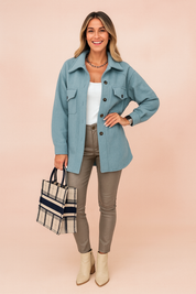 Light blue button-up wool jacket with flap pockets, paired with a white fitted tank top, taupe slim-fit leather pants, plaid tote bag, and cream ankle boots for a chic casual look.