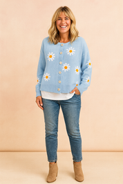 Light blue cardigan with white daisy prints and yellow centers, front button closure, paired with a white undershirt, medium-wash jeans, and taupe ankle boots.