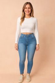 Light blue high-waisted skinny jeggings with faded wash, paired with a fitted white long-sleeve crop top and beige sneakers, styled in a pastel-toned fashion shoot