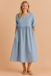 Light blue midi dress with elbow-length sleeves, gathered empire waist, subtle textured weave, side pockets, and soft A-line silhouette.