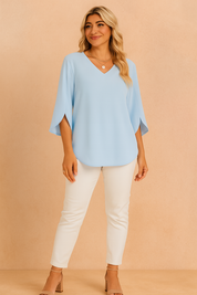 Soft blue V-neck blouse with slit sleeves, paired with white slim-fit pants and nude block-heeled sandals for a fresh and airy spring-summer outfit.
