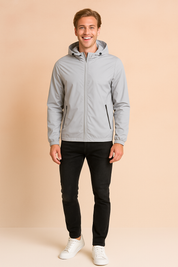 Light gray hooded windbreaker jacket with front zipper, adjustable drawstrings, and zippered side pockets, styled with slim black jeans and white sneakers.