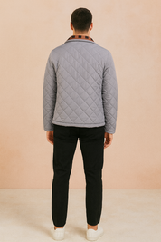 Back view of a light gray diamond-quilted jacket with a straight hem and structured collar, paired with black trousers and white sneakers.
