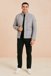 Light gray diamond-quilted jacket with stand-up collar, flap pocket, and snap-button closure, paired with black trousers and white sneakers.