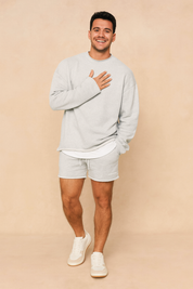 Light grey casual men’s lounge set featuring a relaxed-fit long-sleeve sweatshirt with layered hem detail and matching drawstring shorts for a minimalist streetwear look.