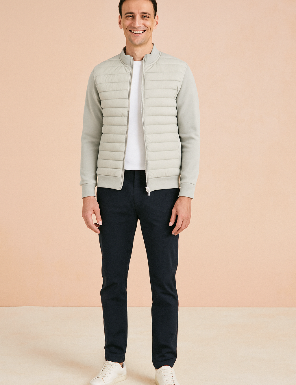 Light grey quilted zip-up jacket with ribbed cuffs and hem, paired with dark trousers and white sneakers.