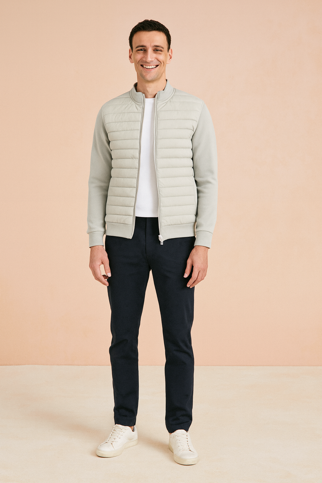 Light grey quilted zip-up jacket with ribbed cuffs and hem, paired with dark trousers and white sneakers.