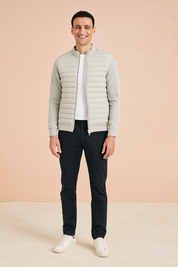 Light grey quilted zip-up jacket with ribbed cuffs and hem, paired with dark trousers and white sneakers.