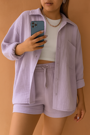 Crinkled lilac loungewear co-ord set featuring a button-up oversized shirt and high-waisted drawstring shorts, styled with a white ribbed crop top and chain necklace.