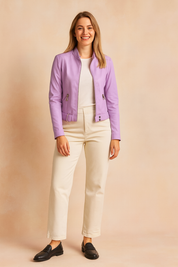 Lilac faux leather jacket with zippered front pockets, belted waist detail, and button closure, paired with cream trousers and black loafers for a chic modern look.