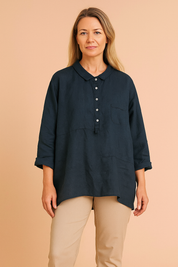 Navy blue linen women's shirt with collar and buttons, modeled by a European woman with long ash blond hair, fashion photography on a soft sand pink background.