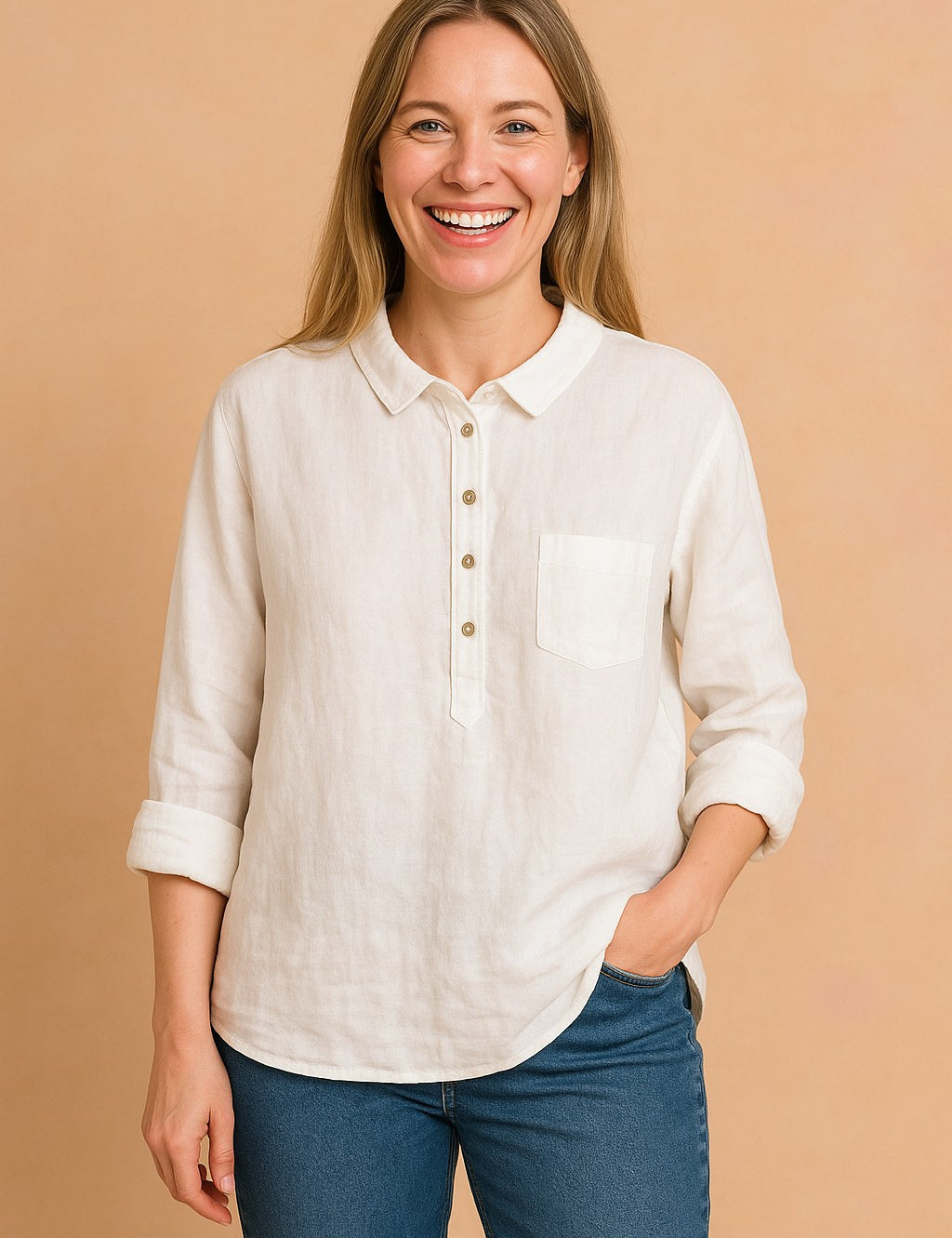 European woman with ash blond hair wearing a crisp white linen shirt and blue jeans, standing against a soft sand pastel background.