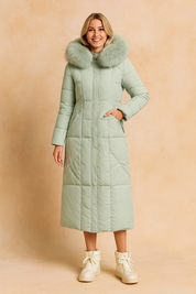 Long light green winter parka coat with large fur-trimmed hood, quilted pattern, and zip closure, styled with high-top winter boots.