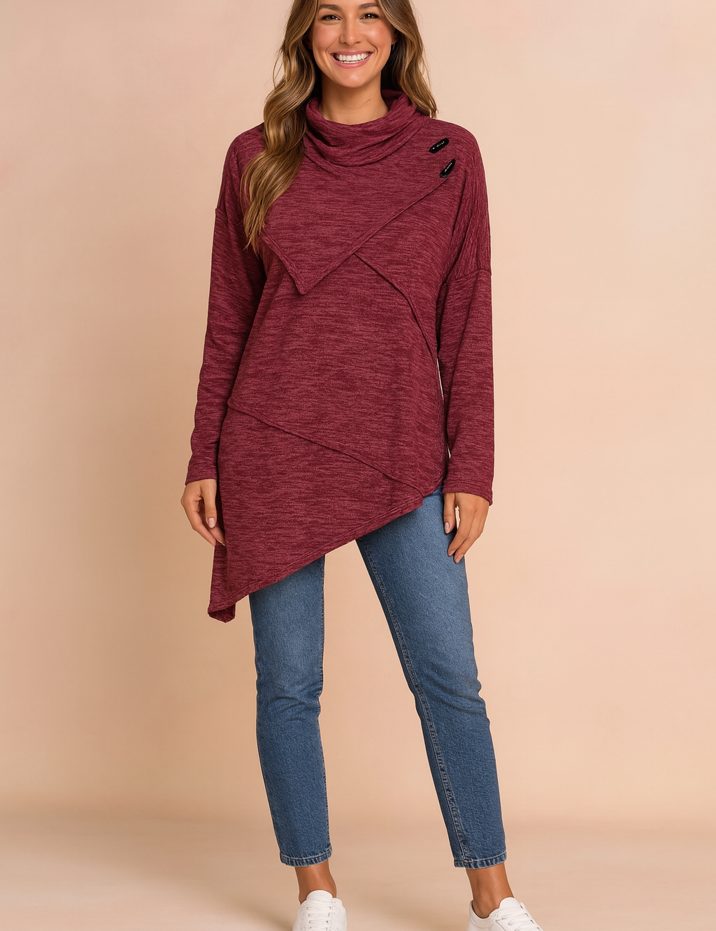 Maroon asymmetrical cowl-neck tunic sweater with black button details, paired with mid-rise blue skinny jeans and white low-top sneakers.