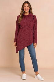 Maroon asymmetrical cowl-neck tunic sweater with black button details, paired with mid-rise blue skinny jeans and white low-top sneakers.