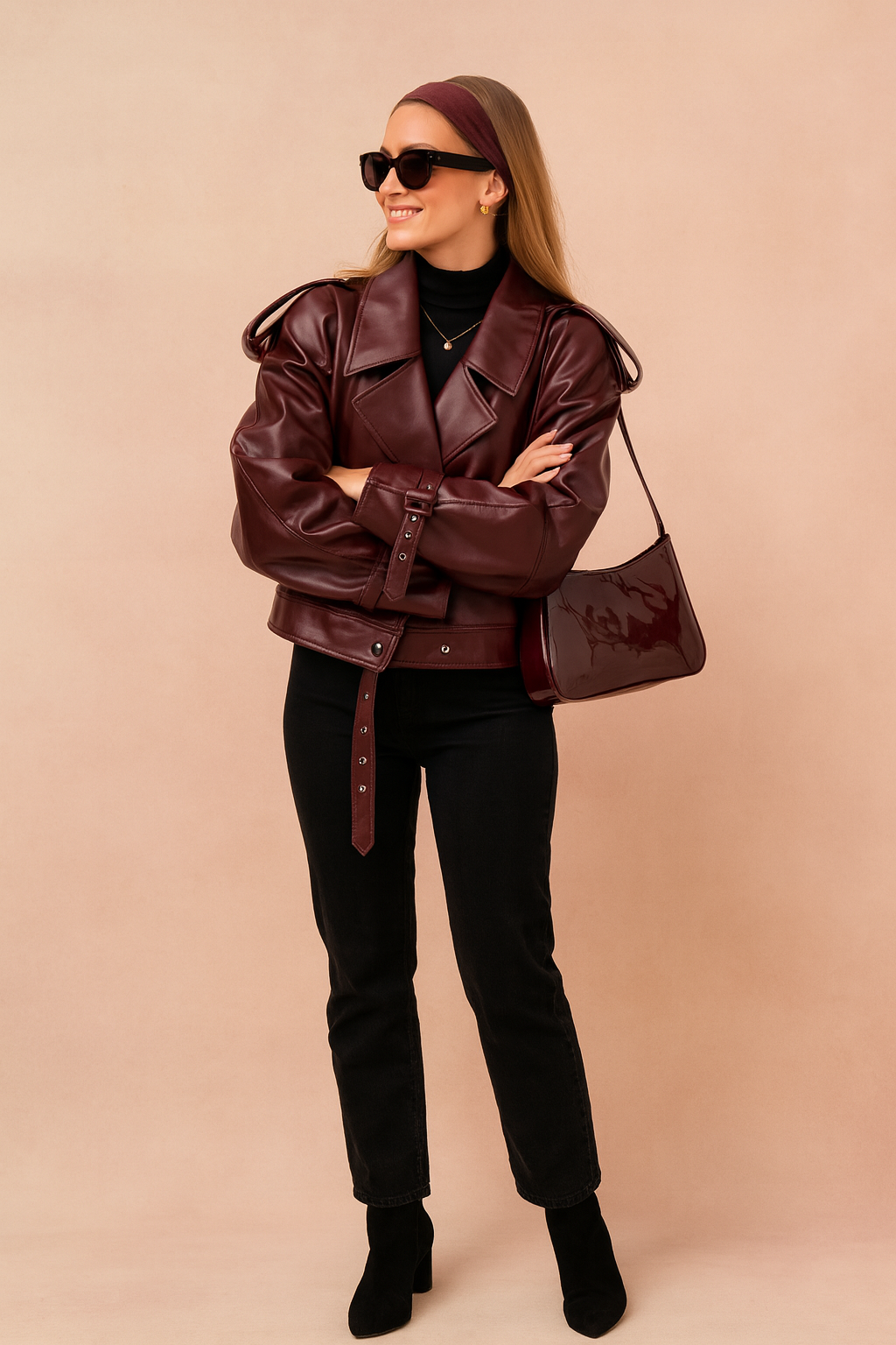 Oversized maroon leather jacket with wide lapel collar, belted cuffs, and waist strap, paired with black high-waisted jeans and heeled ankle boots.