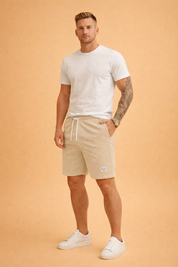 Men’s beige corduroy casual shorts featuring a soft ribbed cotton fabric, elastic waistband with white drawstring, relaxed straight-leg cut, side pockets, and a minimalist woven label detail, maintaining a clean summer-ready silhouette with consistent rib texture and natural beige tone.