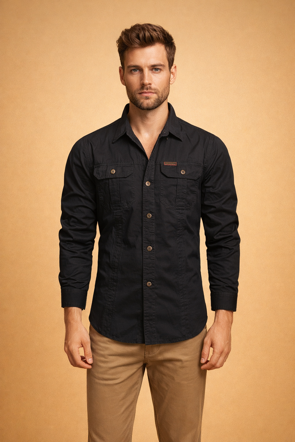 Men’s black long-sleeve button-up shirt with structured collar, front button closure, dual chest flap pockets with buttons, tailored fit, paired with straight-cut beige trousers.