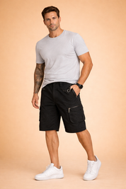 Men’s black utility cargo shorts made from durable matte fabric, featuring multiple zippered and flap pockets, reinforced panel construction, metal D-ring waist detail, secure button closure, straight knee-length cut, and structured seams designed for outdoor and everyday wear.