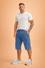 Men’s knee-length blue cargo shorts crafted from smooth woven performance fabric with a matte finish, featuring a structured waistband with single button closure, zip fly, belt loops, angled side pockets, a secure zip pocket, and a utility cargo pocket with flap and stitched logo patch, paired with a solid burgundy short-sleeve crew-neck T-shirt in soft knit fabric and white athletic sneakers with layered panels and cushioned soles.