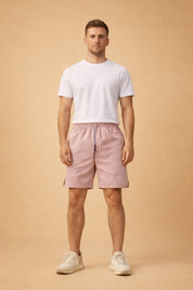 Light dusty-rose men’s summer shorts with elastic waistband and drawstring, paired with a clean neutral short-sleeve shirt and minimalist low-profile sneakers for a modern casual outfit