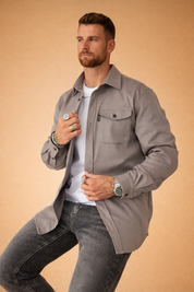 Modern men’s long-sleeve overshirt layered over a fitted crew-neck top, featuring a structured collar, button-front closure, single chest flap pocket, straight hem, and paired with slim straight-leg jeans for a clean, contemporary look.