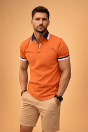 Men’s fitted orange short-sleeve polo shirt with contrast navy-and-white collar and sleeve cuffs, three-button placket, smooth structured fabric, paired with beige tailored chino shorts with flat front and clean hem